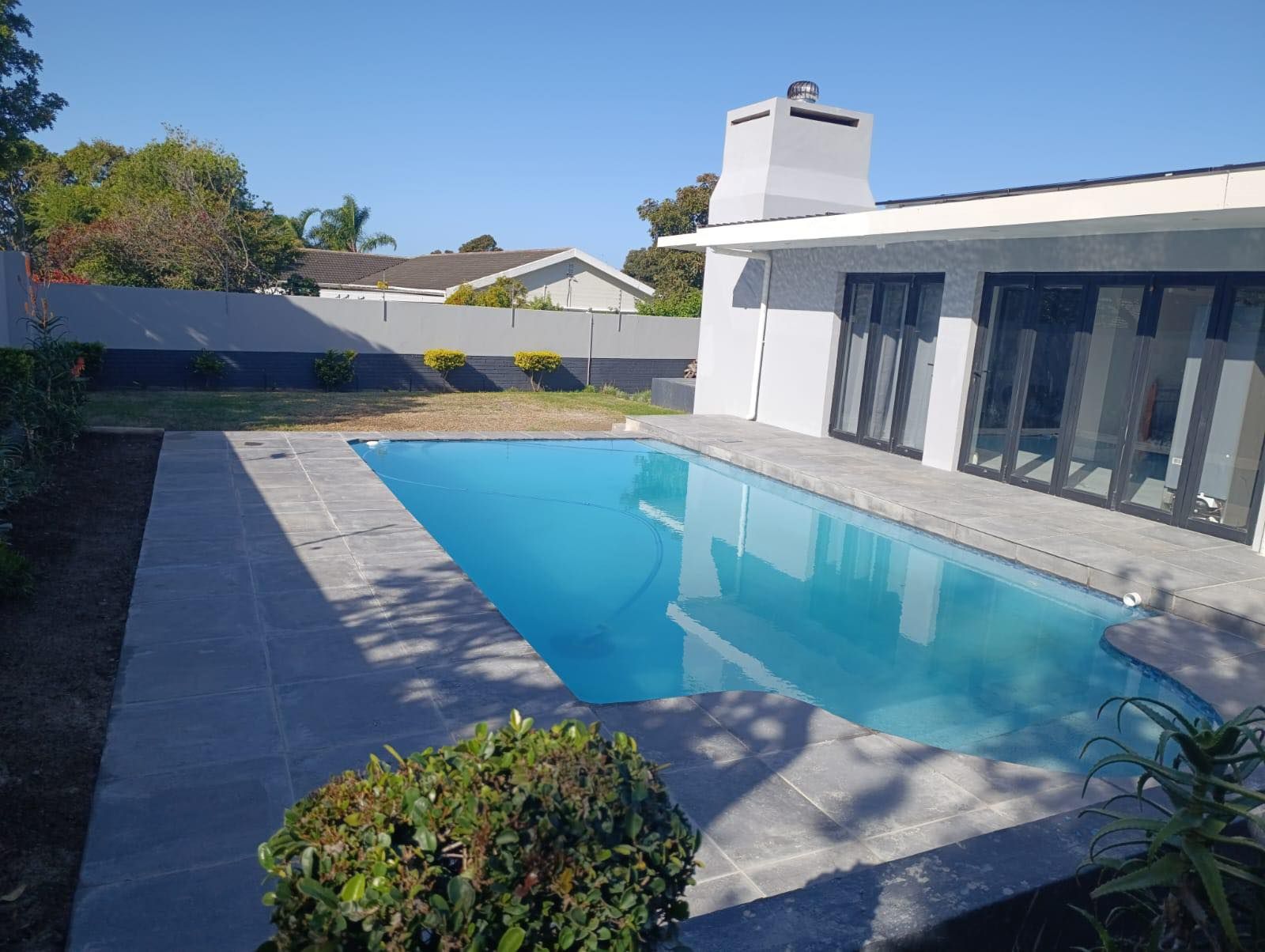 Completed crystal-clear swimming pool beside modern home built in Port Elizabeth by NHBRC certified pool builders